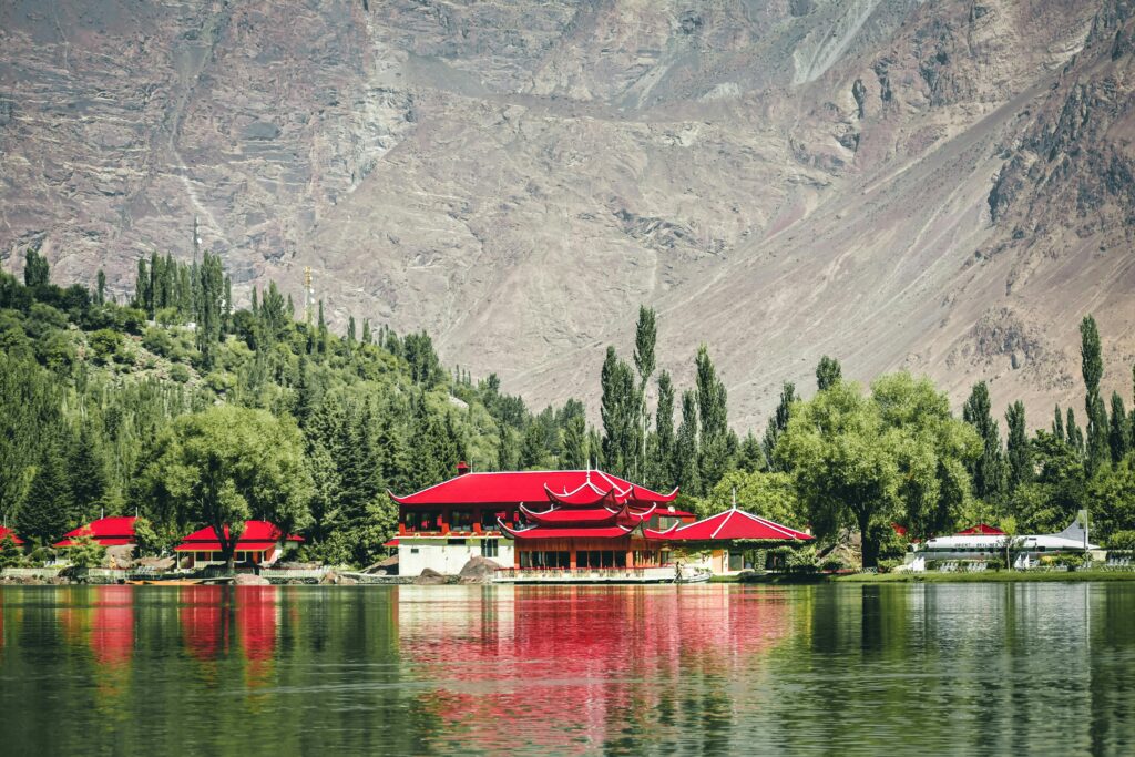 Stunning lake view with traditional architecture and vibrant red roofs framed by mountains and trees.