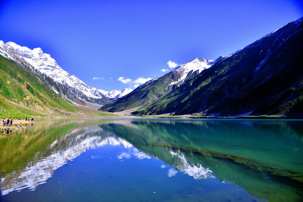 Breathtaking view of a reflective lake in Kaghan Valley, Pakistan, surrounded by snow-capped mountains.