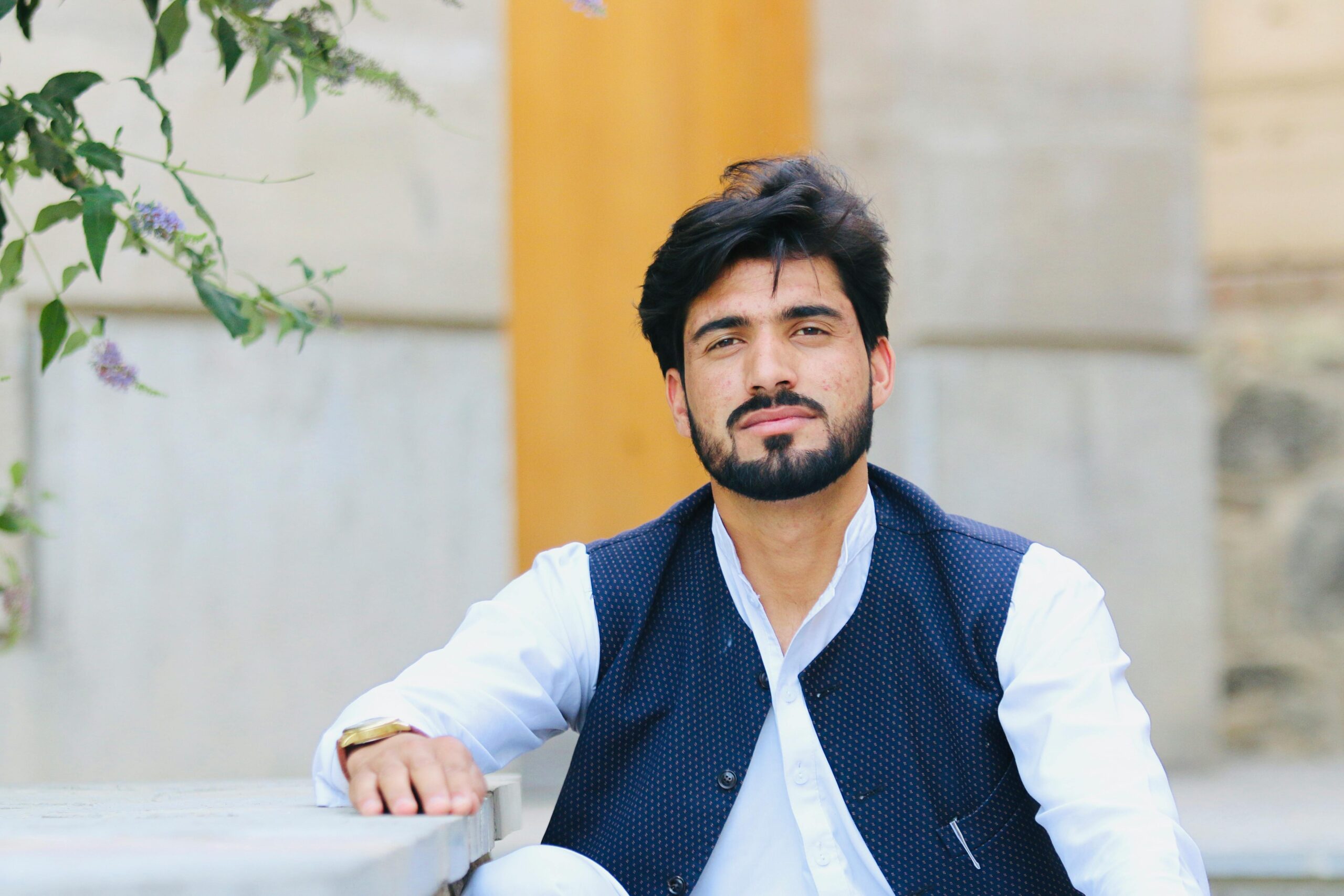 A portrait of a bearded man in traditional attire sitting outdoors with a serene expression.