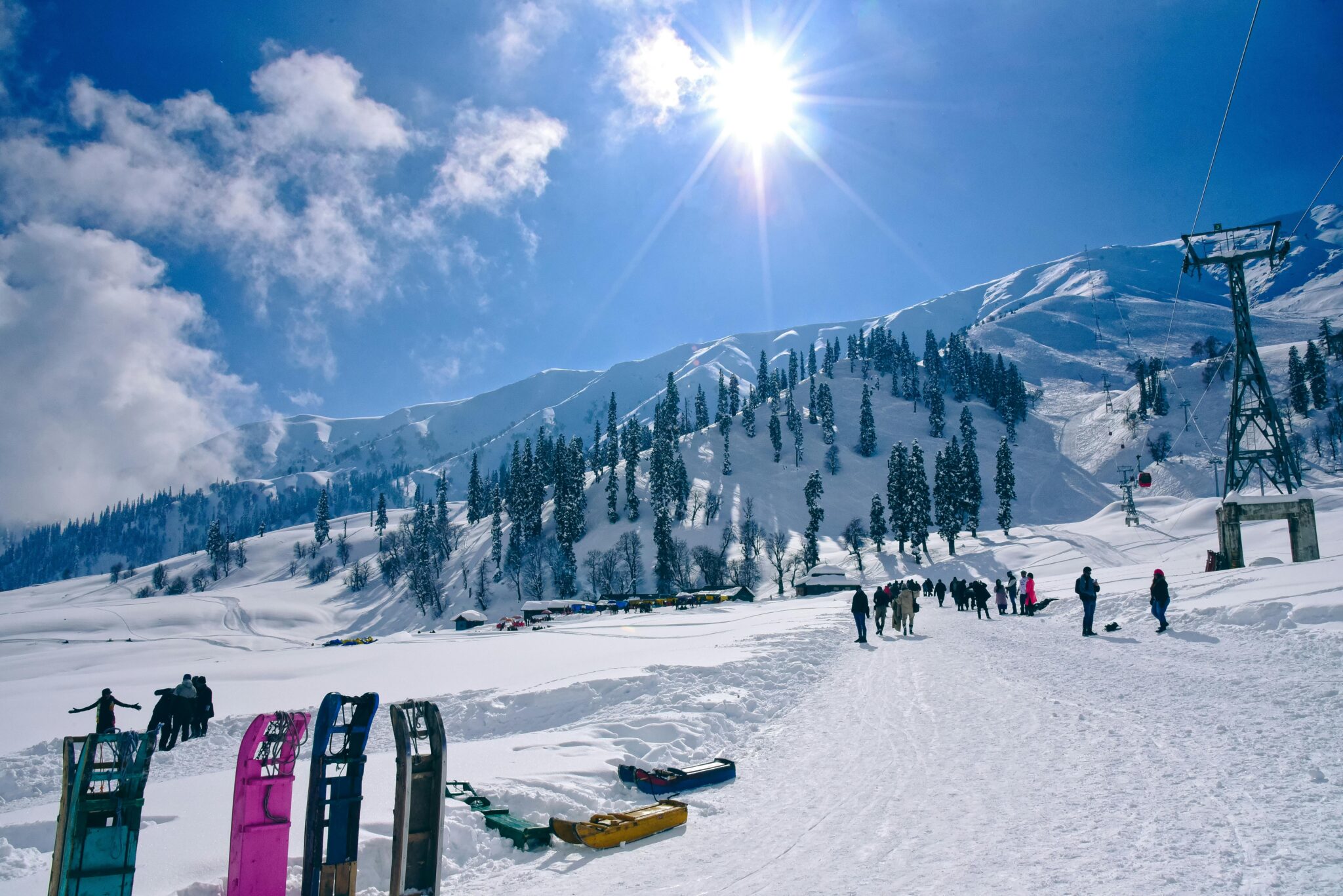 Explore a scenic winter landscape with sunlit snowy mountains and coniferous trees against a bright blue sky.