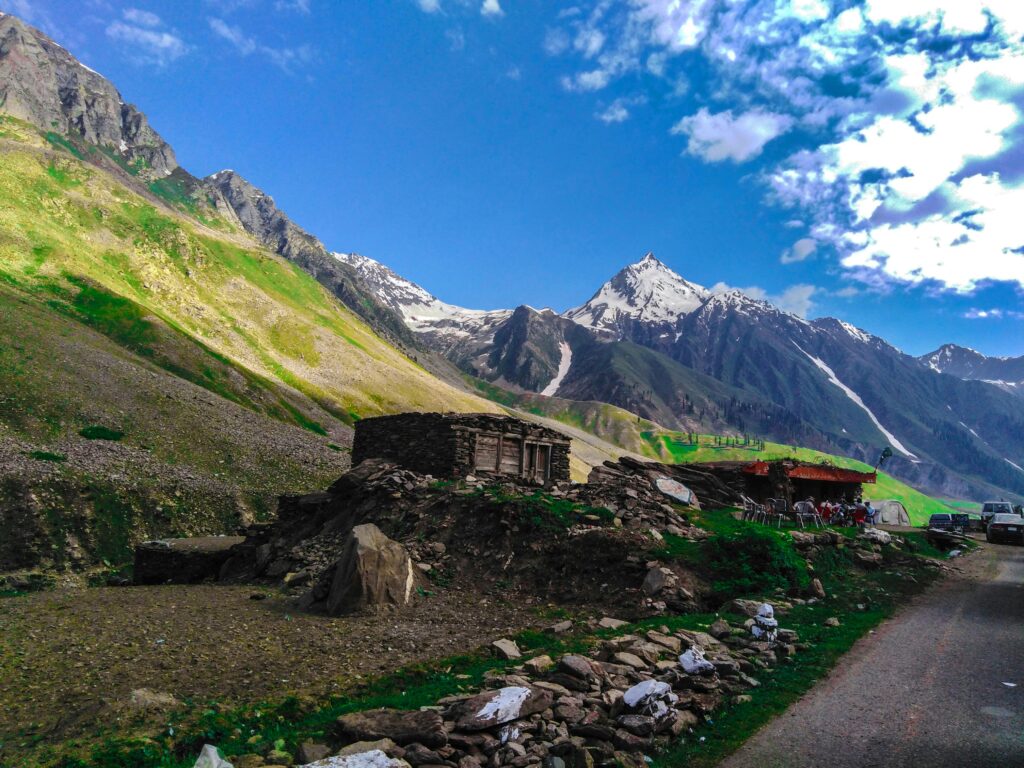 Scenic view of rocky mountains and green fields in rural Pakistan with blue skies.